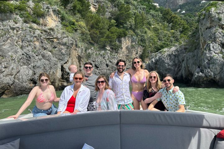 Group of people on a boat in front of rocky cliffs and greenery.