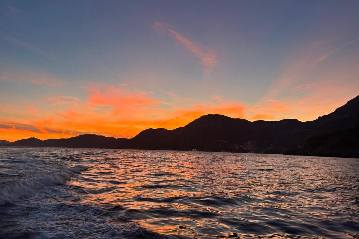 Sunset over mountains with vibrant orange sky reflecting on ocean waves.