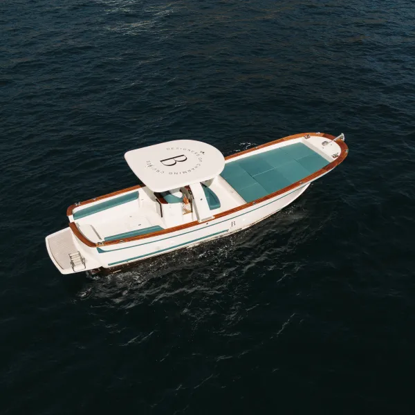 Aerial view of a small white yacht with teal deck on dark water.