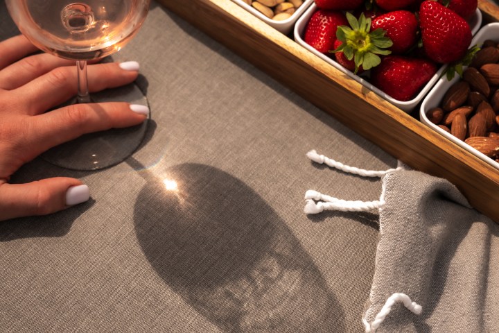 Hand holding wine glass, snacks in dish, on gray fabric with shadow.