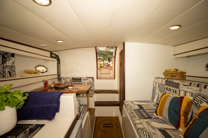 Interior of a cozy boat cabin with a dining table and colorful cushions, view outside.