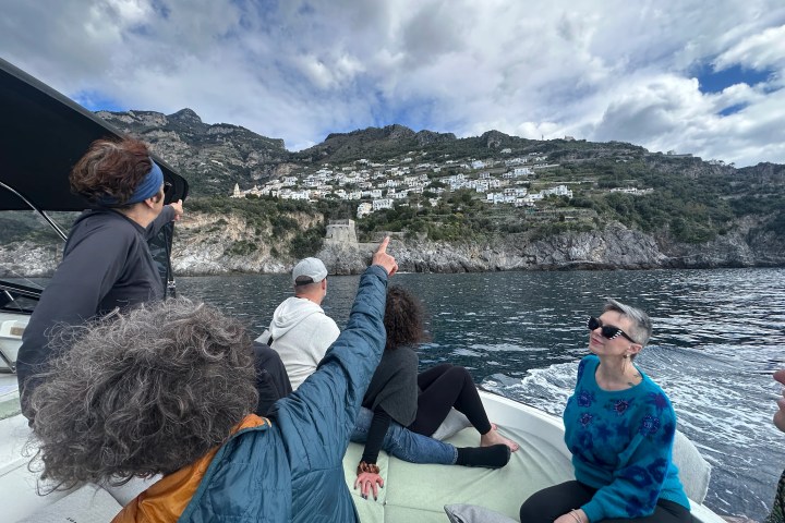 People on a boat pointing at hillside town across the water.