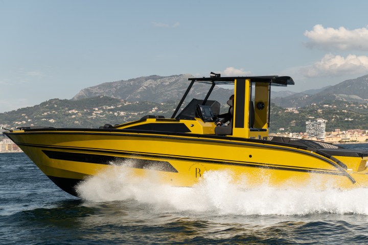 Yellow speedboat moving fast on water with mountains and a cityscape in the background.