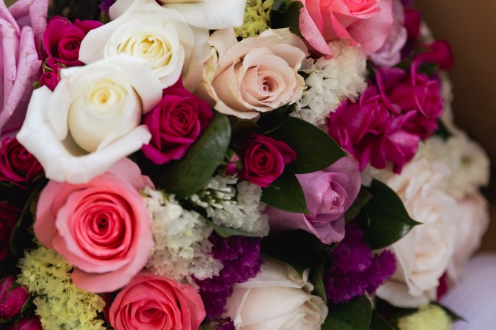 Colorful bouquet of assorted roses and flowers on tan surface.