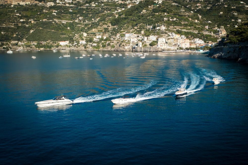 Four motorboats creating wakes on blue water near a coastal town.