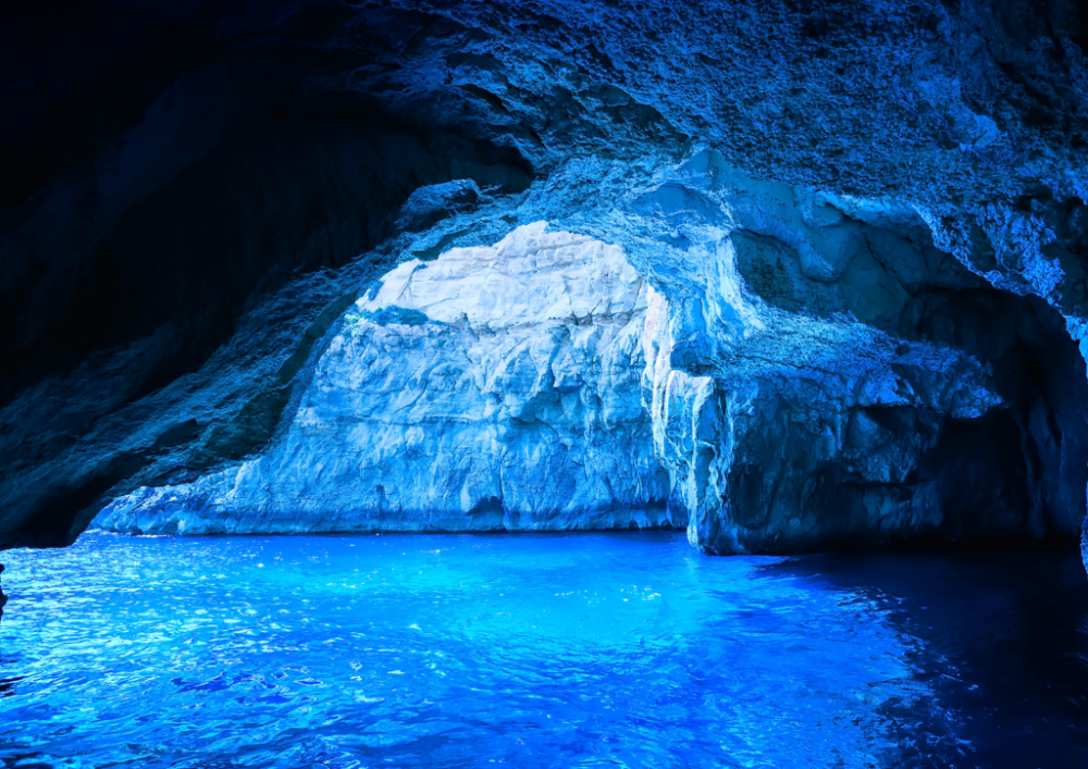 Blue-lit sea cave with bright water and rocky ceiling.