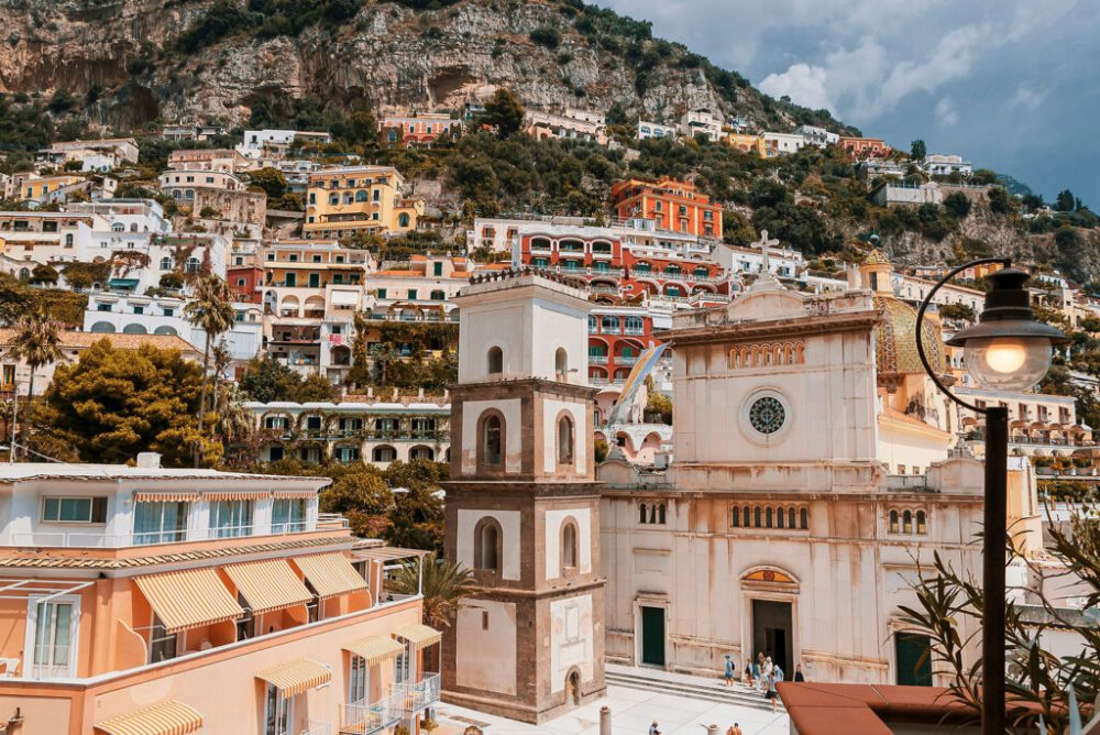 Colorful hillside houses and a church facade in Positano, Italy, with a rocky cliff backdrop.