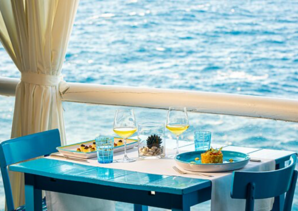 Outdoor dining table for two by the sea with blue chairs and nautical decor.