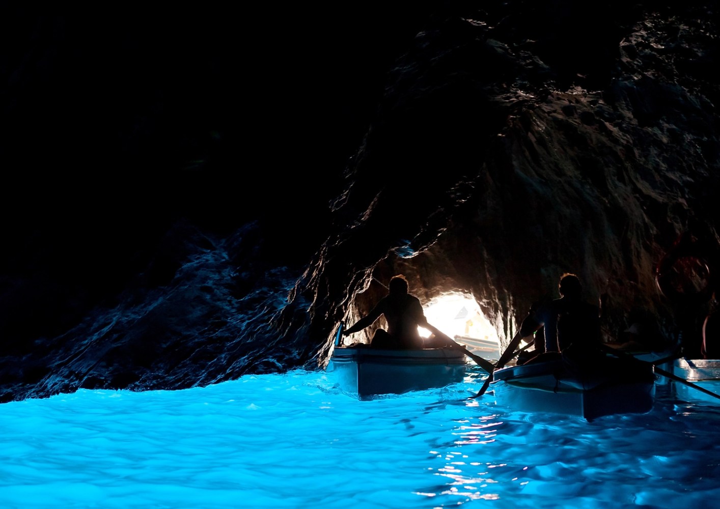 Boats entering a dark cave with vibrant blue water and light at the entrance.