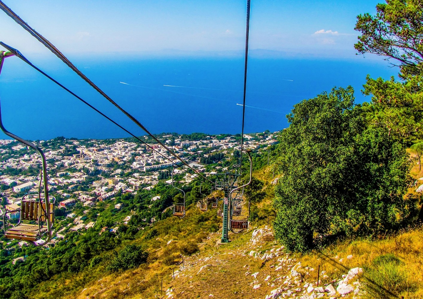 Chairlift ascending a hillside with ocean and town view in the background.