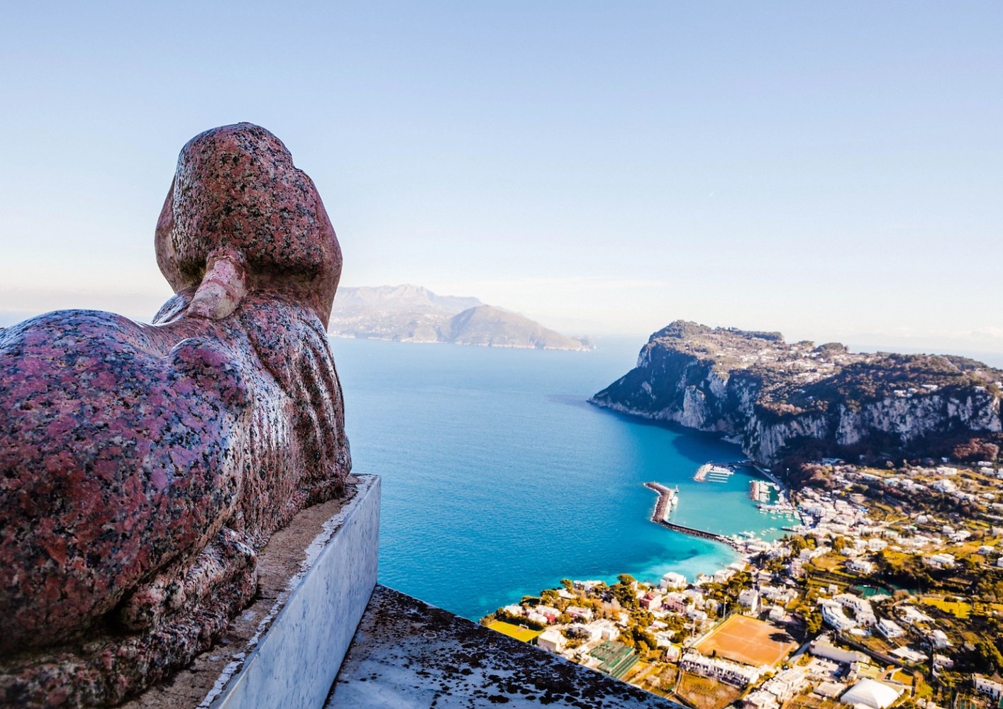 Stone sphinx overlooking a coastal landscape with cliffs and blue sea.