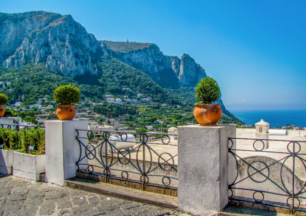 Terrace with potted plants overlooking a coastal mountain landscape and blue sky.