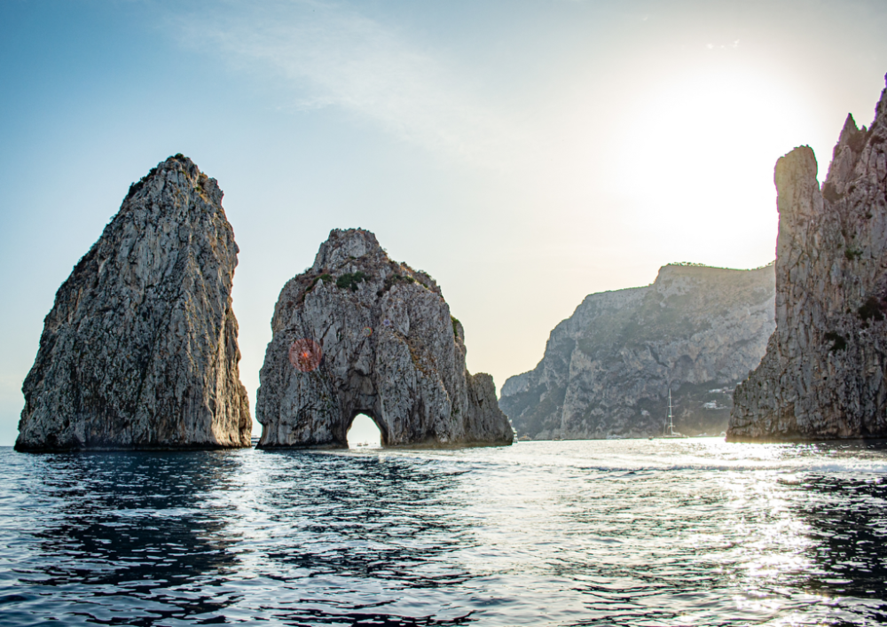 Sea arch rock formations in sunlight, with calm water and clear skies.