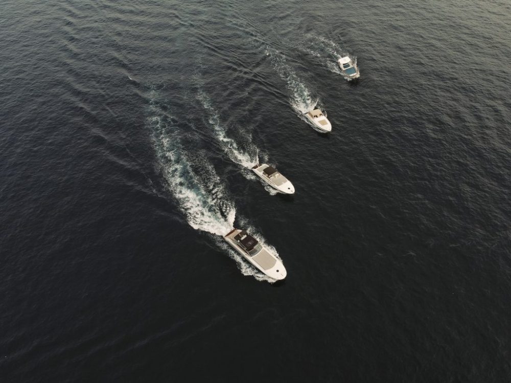 Four boats creating wake in dark water, moving in a line.