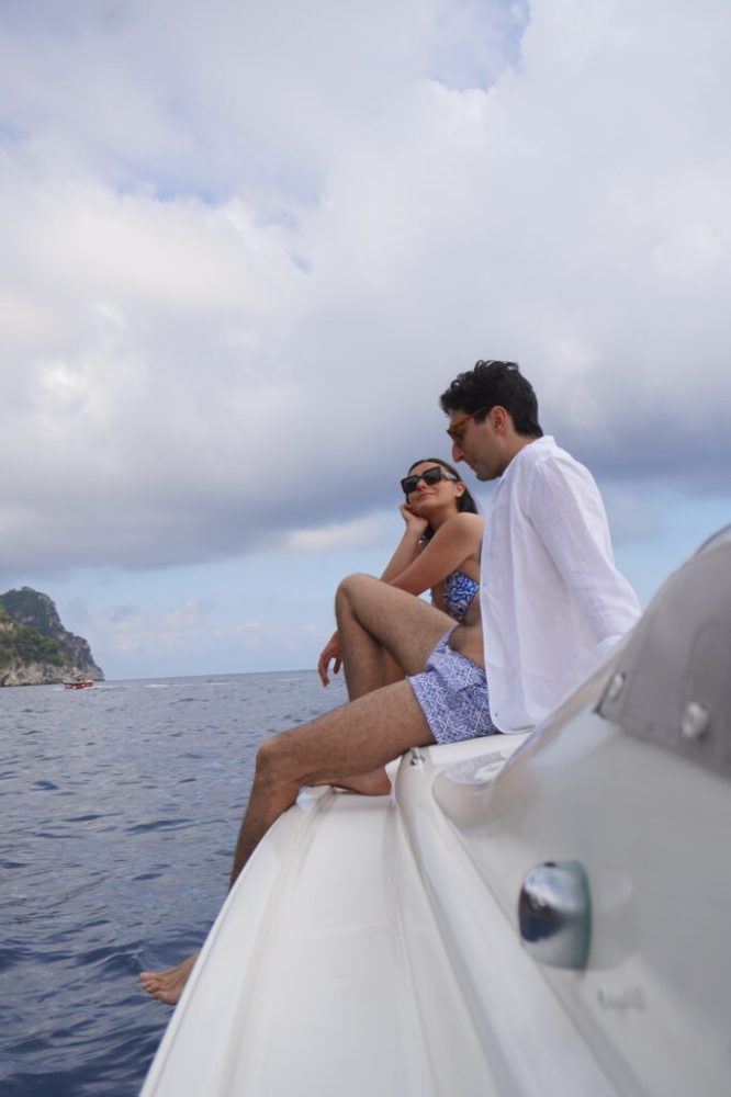 A couple sitting on a boat's edge, looking at the ocean under a cloudy sky.