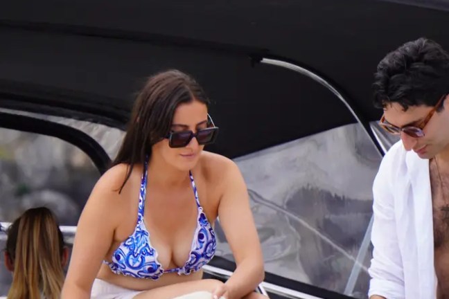 Two people on a boat holding beige towels with a scenic background.