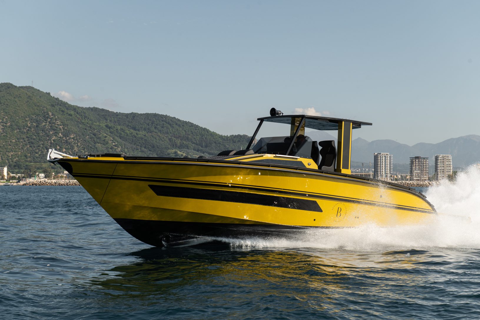 A yellow motorboat speeding on water with a cityscape and mountains in the background.