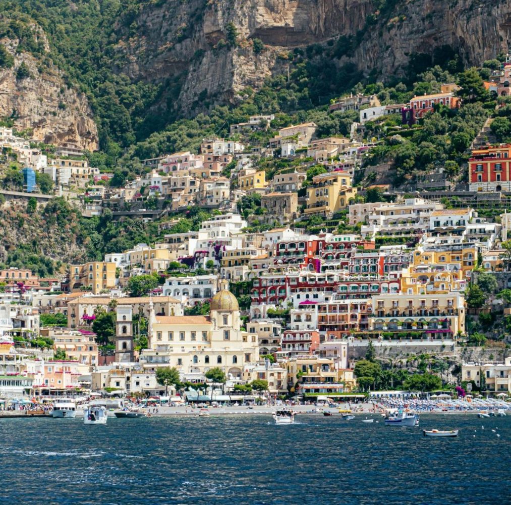 Colorful hillside village by the sea with numerous buildings and a dome.