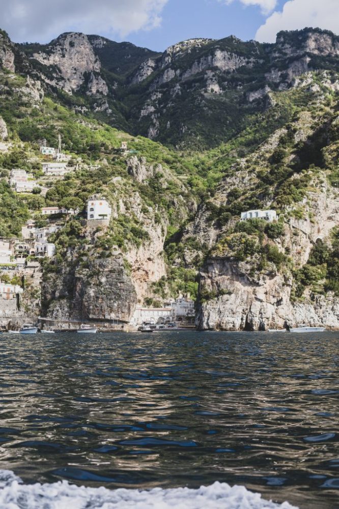 Rocky coastal landscape with cliffs, greenery, and buildings viewed from the water.