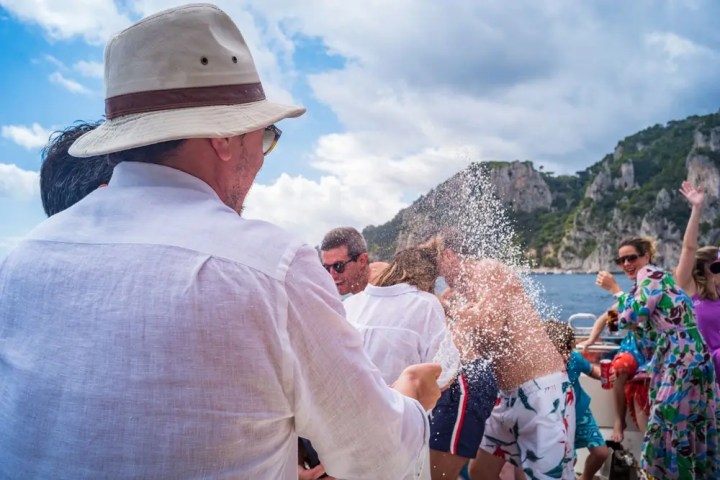 People having fun on a boat, splashing water with scenic cliffs in the background.