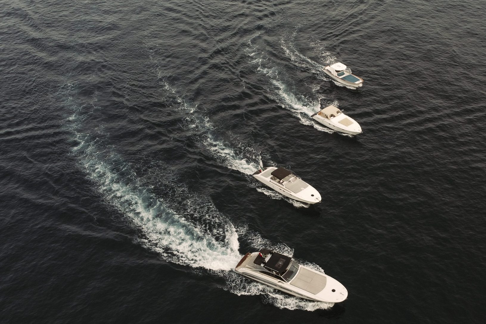Four motorboats speeding on dark water, leaving white wakes behind.