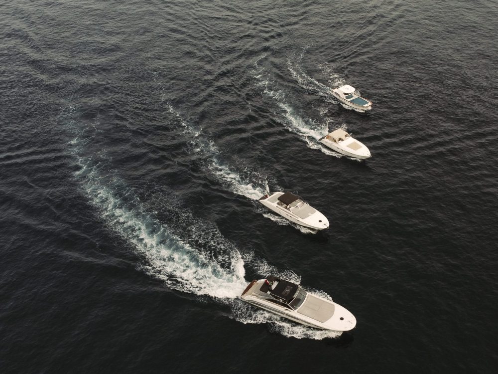 Four motorboats sailing in a line on open water, creating white wakes.