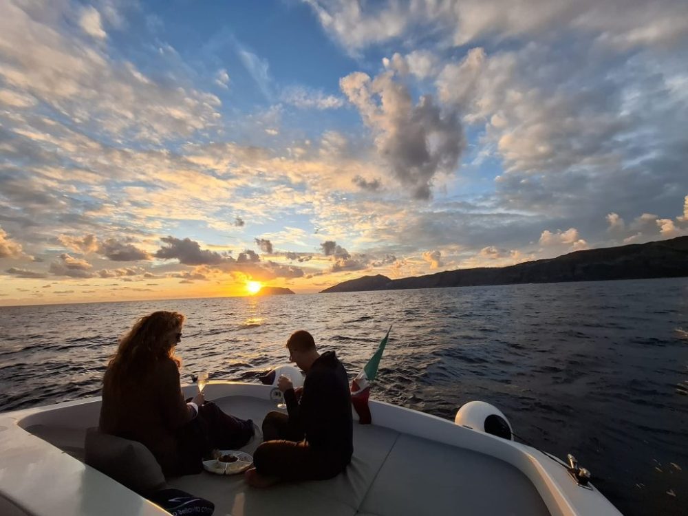 Two people on a boat at sunset, with a view of ocean and clouds.