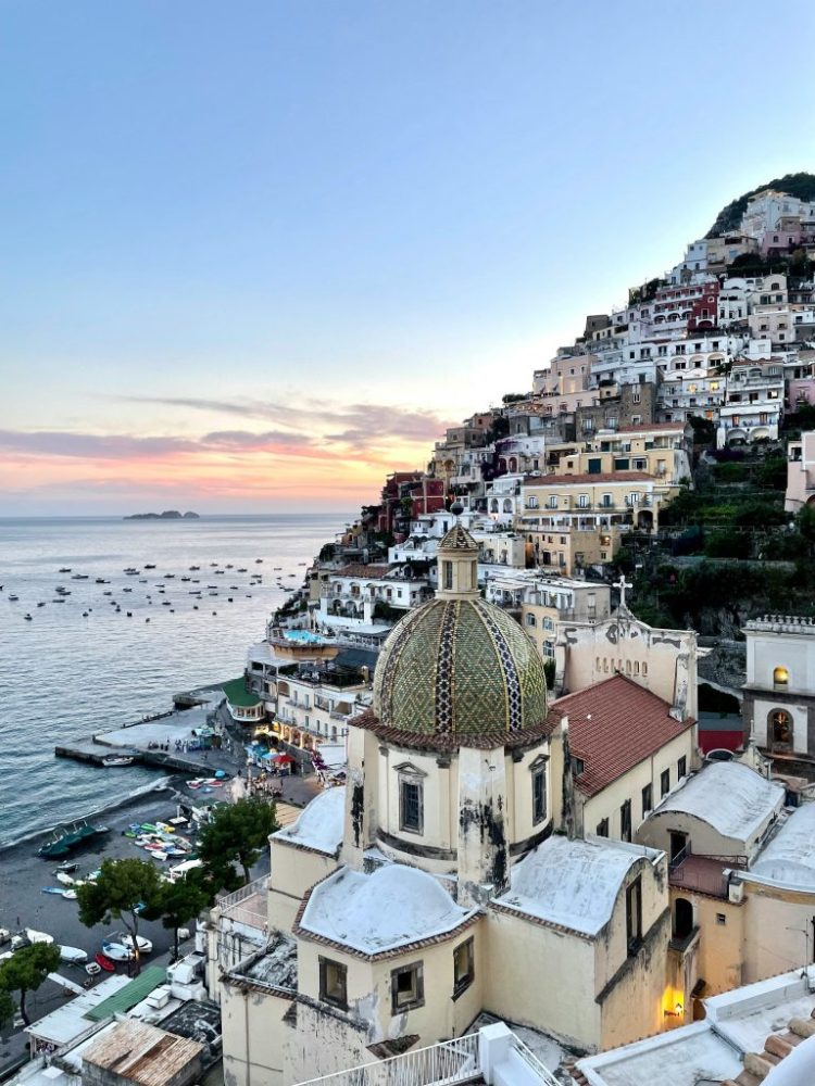 Scenic view of Positano's colorful hillside and coastal sunset with boats on the water.