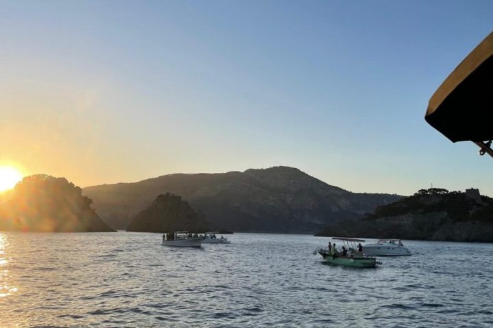 Boats on a lake at sunset, with mountains in the background.