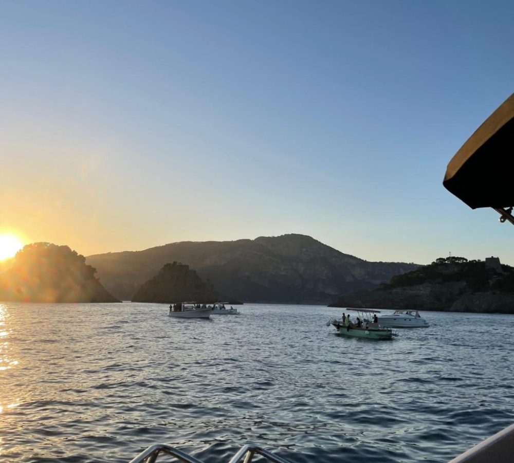 Boats on a lake at sunset, with mountains in the background.