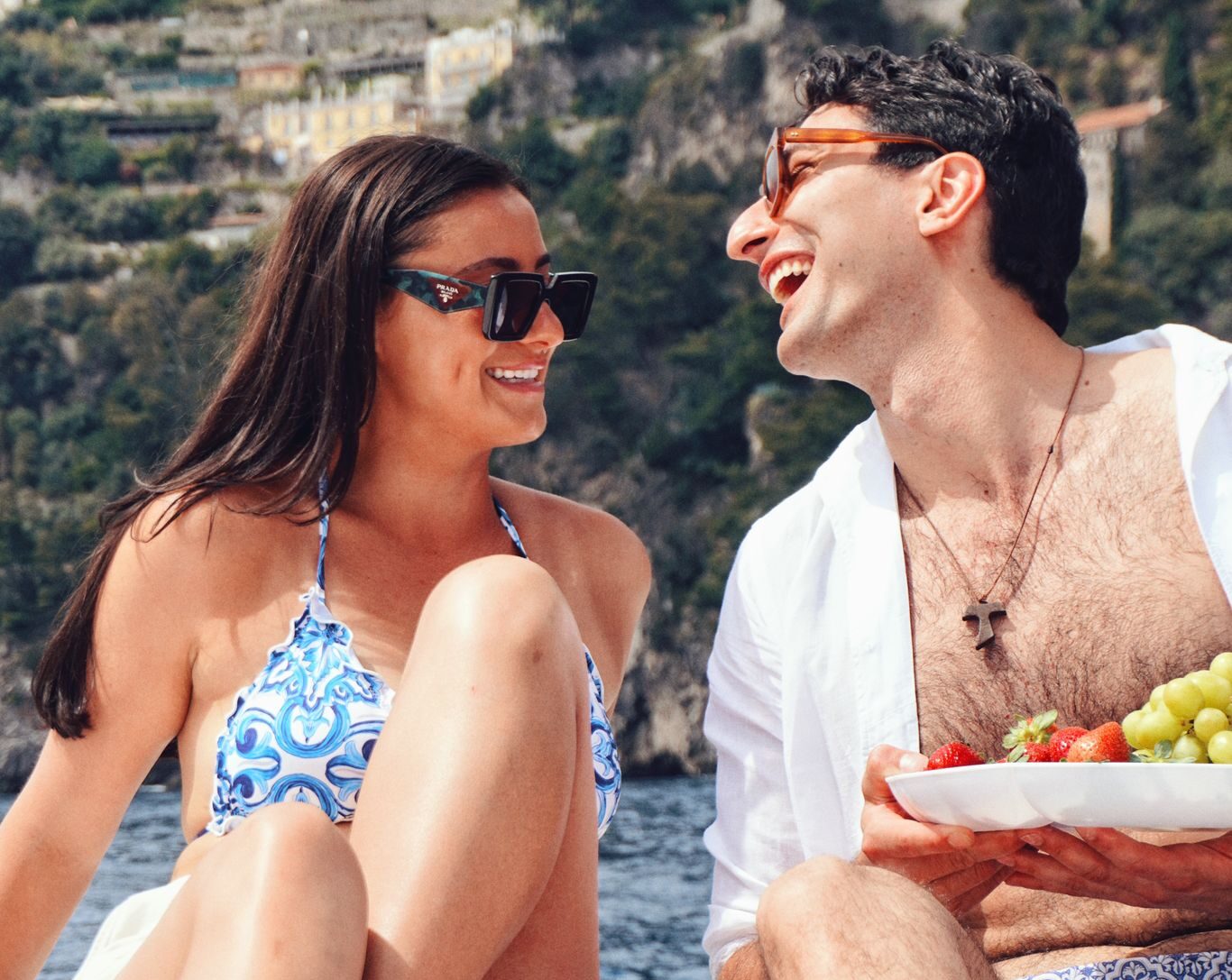 A couple laughing and wearing sunglasses on a boat with fruit in the foreground.