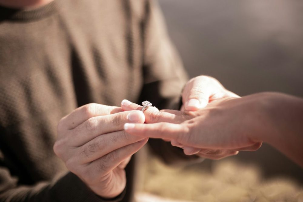 Person placing a ring on another's finger during a proposal.