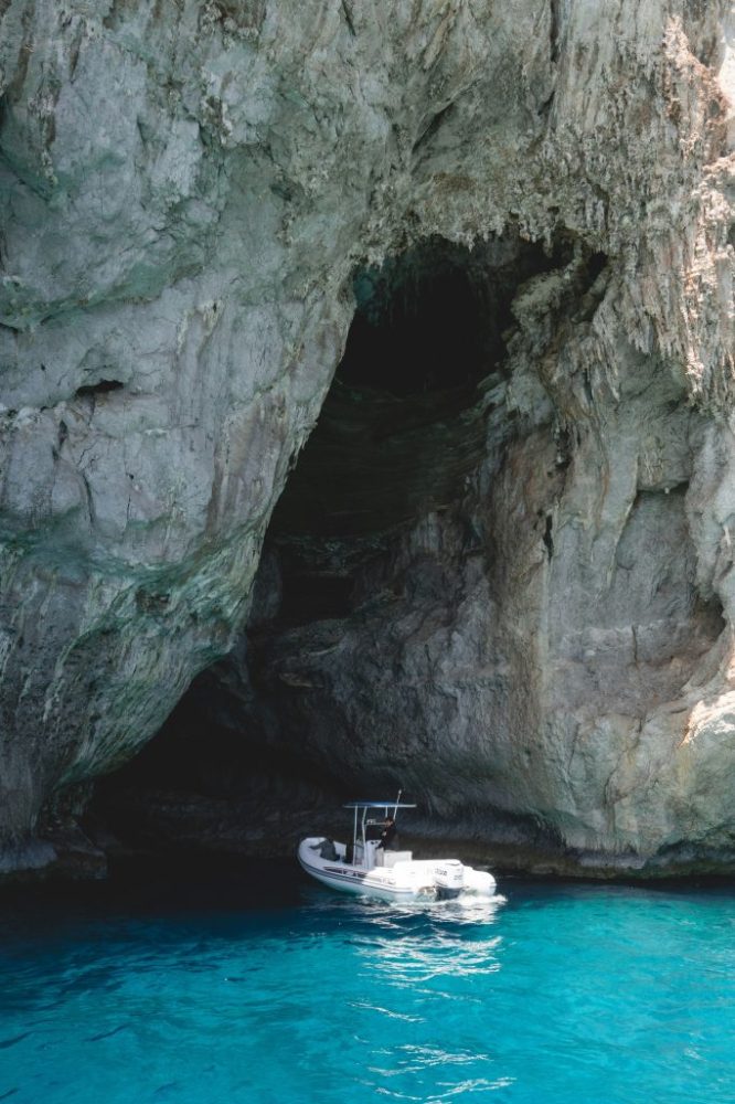 Boat near a cave entrance on a rocky coastline with blue water.