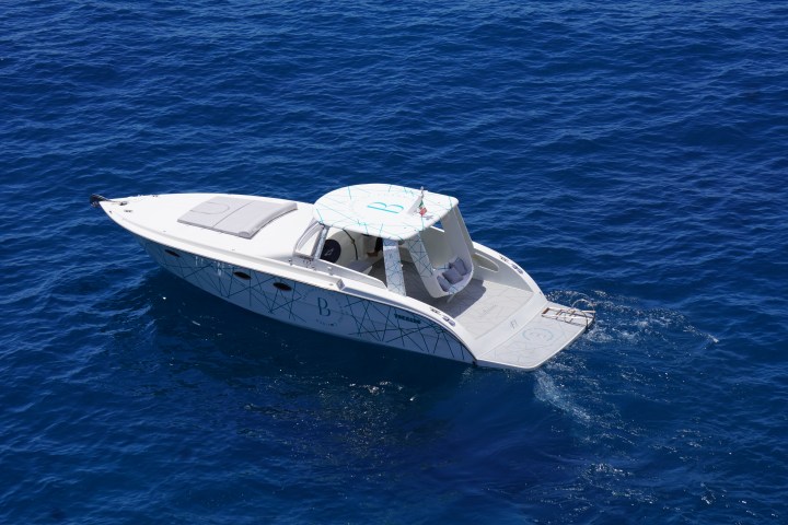 White speedboat with cushions cruising on deep blue water under clear sky.