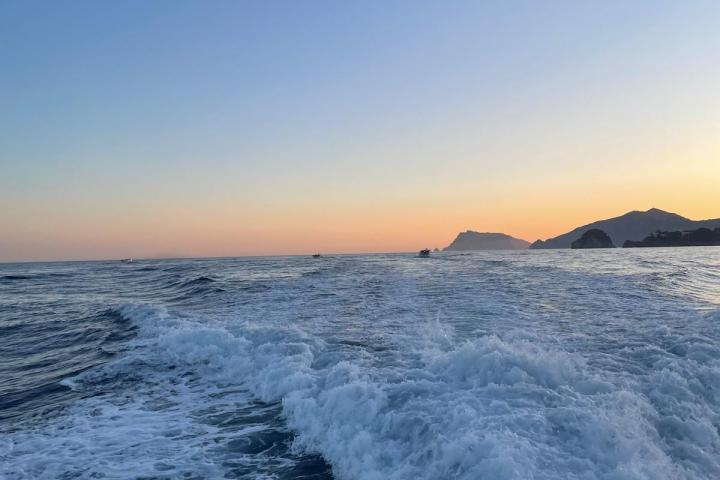 Ocean waves and distant mountains at sunset under a clear sky.