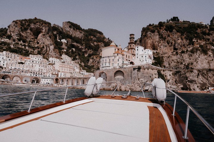 View from a boat approaching coastal cliffs and hillside village with arched buildings.