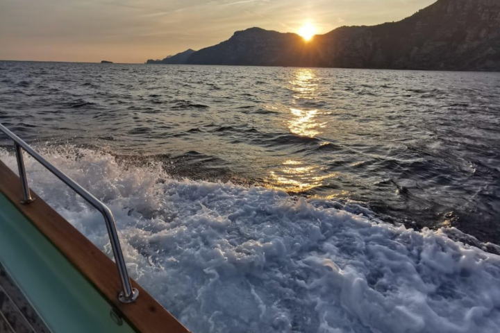View from boat of sunset over mountains and ocean waves.