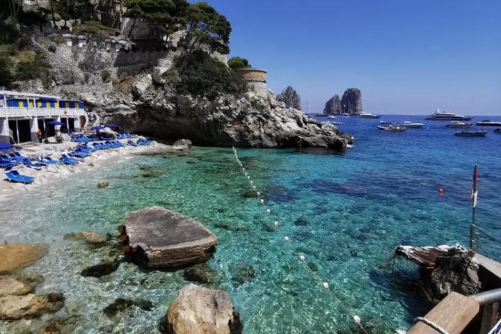 Clear blue sea with rocky shore and distant cliffs under a bright sky.