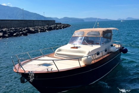 Small boat with canopy docked by rocky shore in sunny weather.