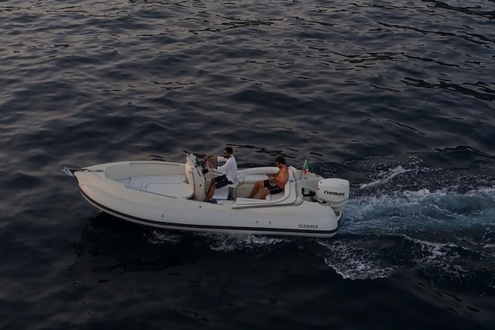 Small motorboat on dark water with two people onboard, creating a wake.