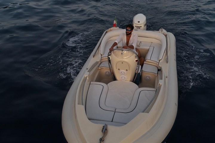 Small motorboat on calm sea near rocky coastline.