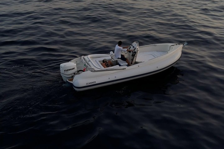 Small motorboat with two people on calm open water under hazy sky.
